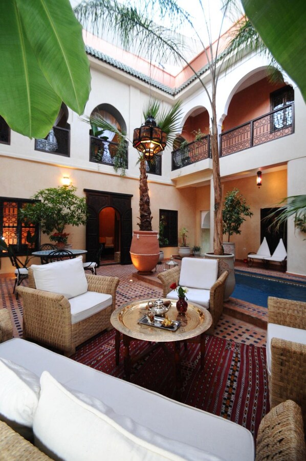 A courtyard with wicker furniture, a central table, and a large potted plant.