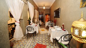 A dining area with tables set for a meal, white curtains, and patterned floor tiles.