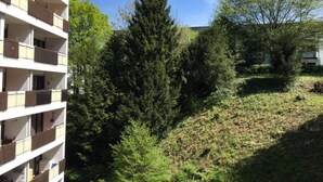En bygning med flere etager og balkoner, omgivet af frodig vegetation og træer.