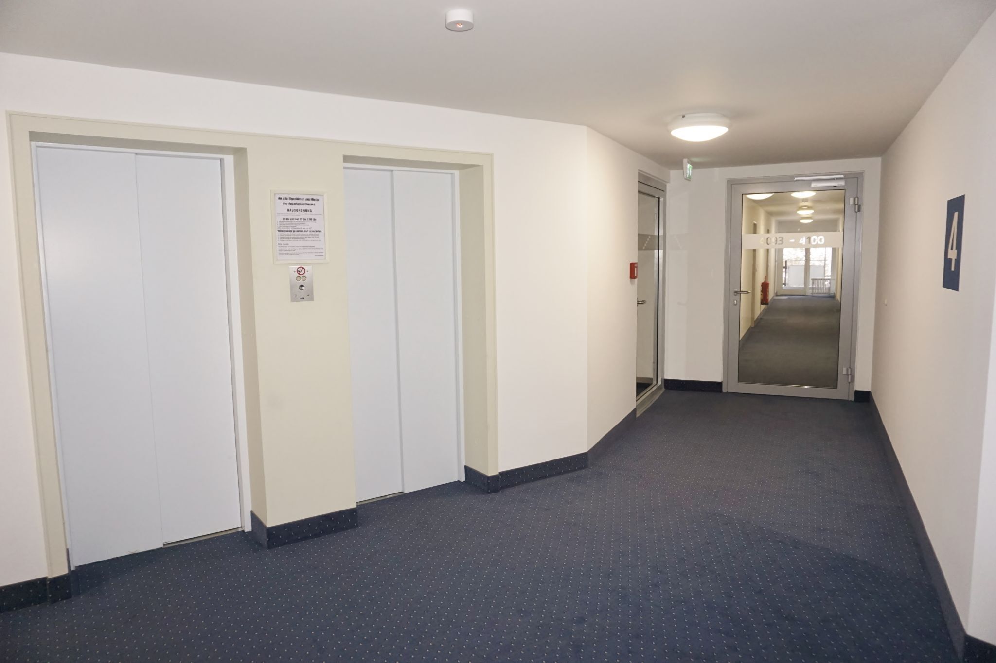 En hall med dörrar, en brandlarm och en korridor som leder till ett annat område.