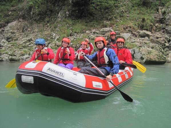 A group of people in a red and white inflatable raft with 'AVANTI' branding, paddling on a calm river surrounded by rocky terrain. - Ferienwohnung Hausberg (Reit im Winkl)