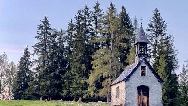Pieni kivikirkko, jossa on kellotorni, ja sen ympärillä on tiheä metsä.