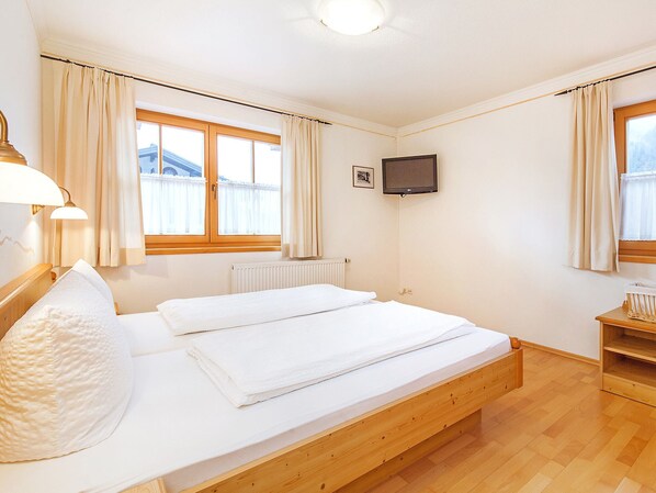 A bedroom with two beds, a TV, and a window with curtains.