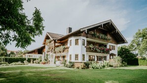 Un edificio de estilo chalete tradicional con varios balcones, rodeado de vegetación exuberante y un césped cuidado.