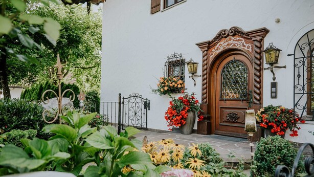 Un edificio blanco con puerta de madera, rejas de hierro forjado y macetas con flores.