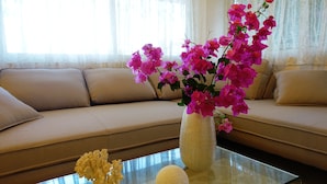 Una sala de estar con un sofá color beige, una mesa de centro de vidrio y un jarrón con flores rosadas.