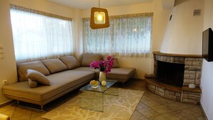Una sala de estar con un sofá, una mesa de centro de vidrio con un jarrón de flores, una chimenea y un televisor montado en la pared.