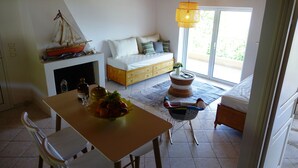 Una habitación acogedora con una mesa de madera, un sofá con cojines, un sillón de mimbre, un pequeño barco modelo y una lámpara de mimbre.