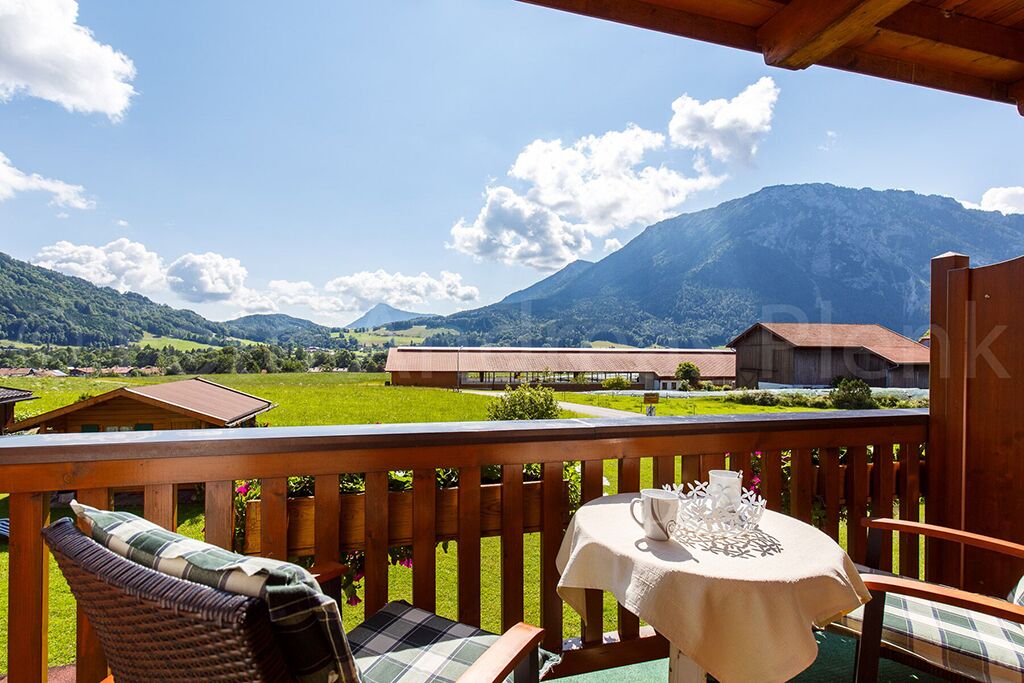 Un balcon agrémenté de fauteuils et d’une table en osier, offrant une vue sur un paysage verdoyant et des montagnes.