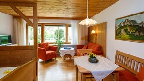 A cozy room with a wooden ceiling, a sofa, a table with a vase of flowers, a television, and a painting on the wall. - Vacation apartment 36 sqm, no. 1, covered terrace, kitchen, 1 living/bedroom, WLAN (Ruhpolding)