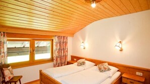 A wooden-paneled bedroom with a double bed, two bedside tables, a chair, and a window with curtains. - Vacation apartment 36 sqm, no. 1, covered terrace, kitchen, 1 living/bedroom, WLAN (Ruhpolding)
