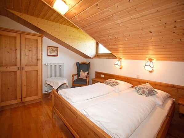 A cozy attic bedroom with a wooden ceiling, a double bed, a chair, and a radiator.