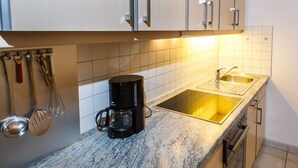 A kitchen with white cabinets, a coffee maker, a sink, and a stove. - Vacation apartment 36 sqm, no. 1, covered terrace, kitchen, 1 living/bedroom, WLAN (Ruhpolding)