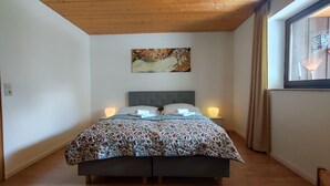 Un dormitorio con una cama, dos lámparas de noche, un cuadro en la pared y una ventana con cortinas.