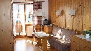 A cozy room with a wooden bed, a wooden desk, a television, and a window with curtains. - (07)Zwei-Raum-Ferienwohnung, 28qm, 2-4 Personen, Extra-Schlafzimer, separate Küche, Balkon (Reit im Winkl)