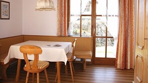 A dining area with a table and chairs, a hanging light fixture, and a window with curtains. - (07)Zwei-Raum-Ferienwohnung, 28qm, 2-4 Personen, Extra-Schlafzimer, separate Küche, Balkon (Reit im Winkl)