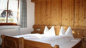 A wooden bed with a headboard, white bedding, and a window with curtains. - (07)Zwei-Raum-Ferienwohnung, 28qm, 2-4 Personen, Extra-Schlafzimer, separate Küche, Balkon (Reit im Winkl)