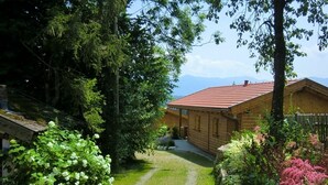 Une cabane en bois avec un toit rouge, entourée d’une végétation luxuriante et un chemin de gravier menant à l’entrée.
