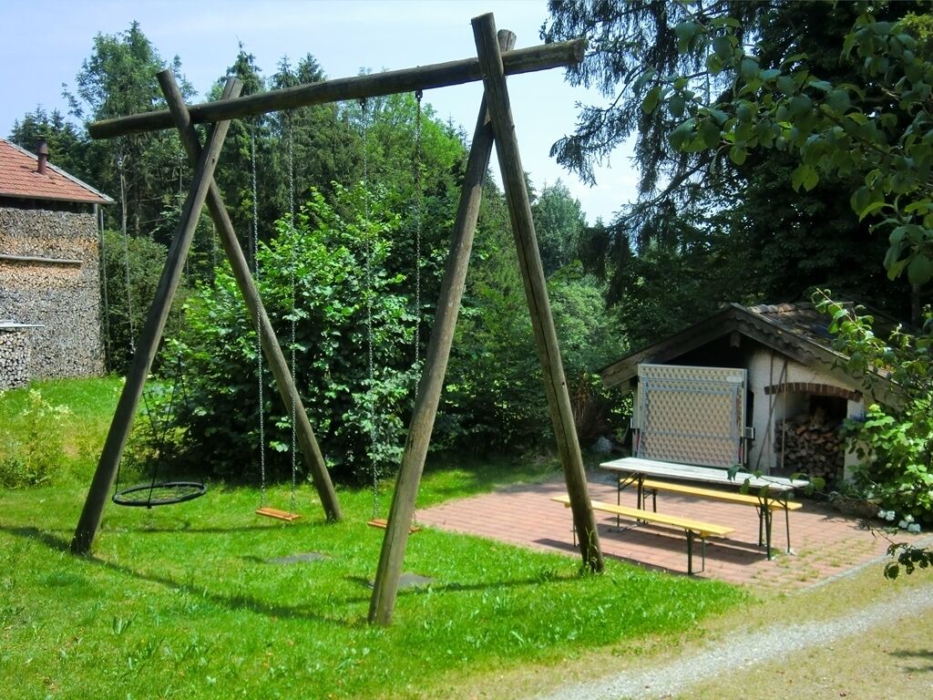 A wooden swing set in a grassy area with a picnic table and a small building in the background.