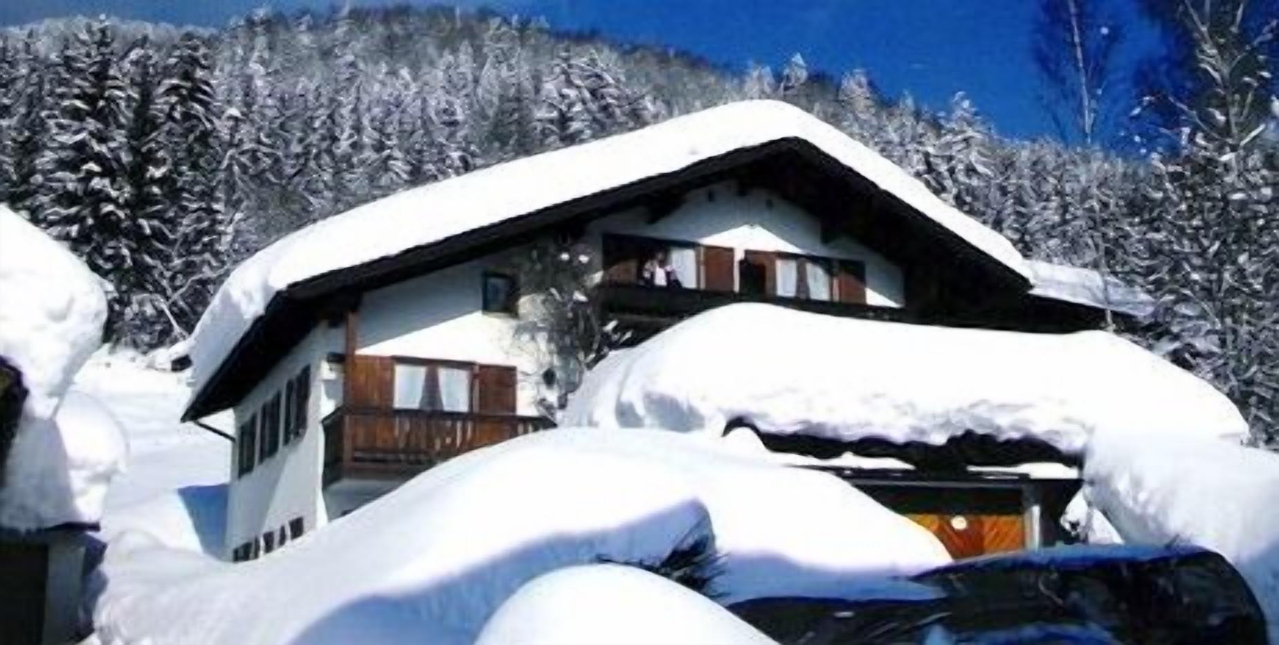 A snow-covered chalet with a wooden balcony, surrounded by snow-laden trees.