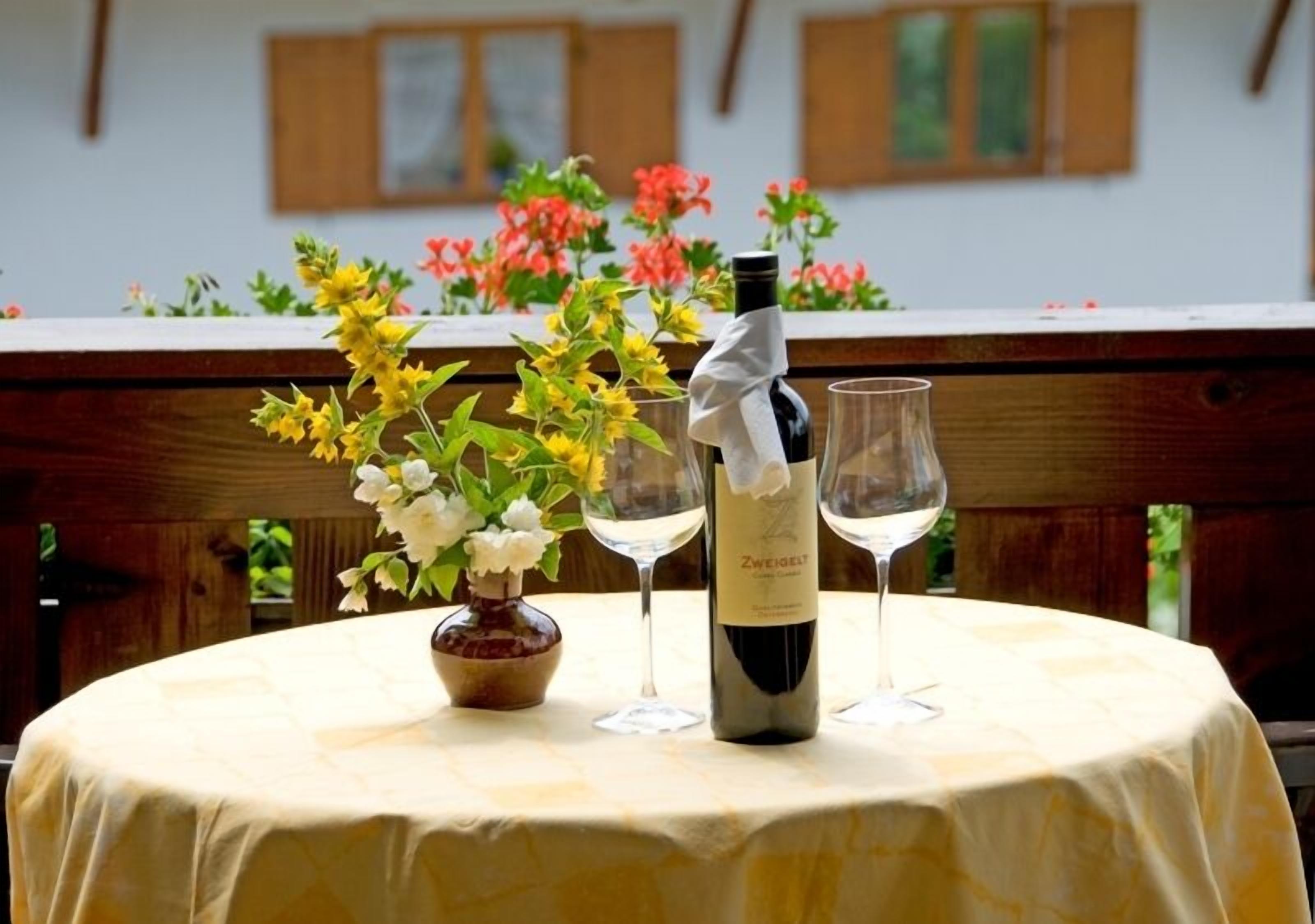 Une table ronde avec une bouteille de vin et deux verres à vin, entourée de fleurs.