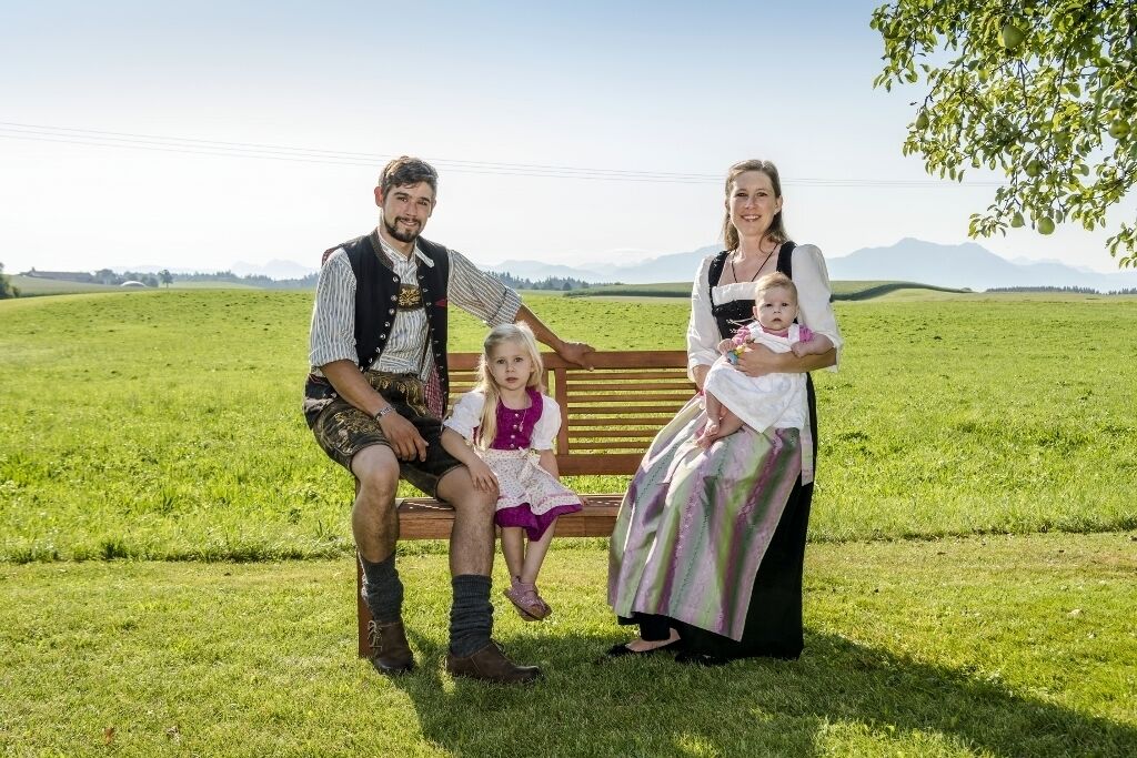 A family of four on a bench in a grassy field with mountains in the background.