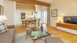 A modern living room with a glass coffee table, a sofa, a TV, and a dining area in the background. - Vakantiewoning Unternberg (Reit im Winkl)