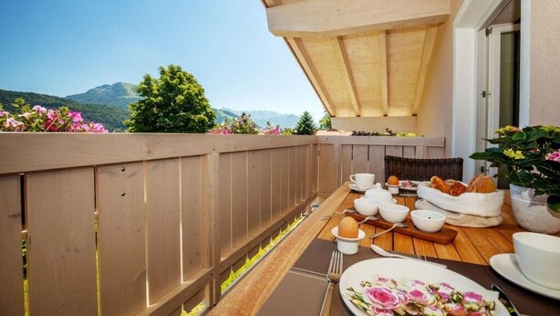 A wooden deck with a table set for breakfast, overlooking a mountainous landscape. - Vakantiewoning Unternberg (Reit im Winkl)