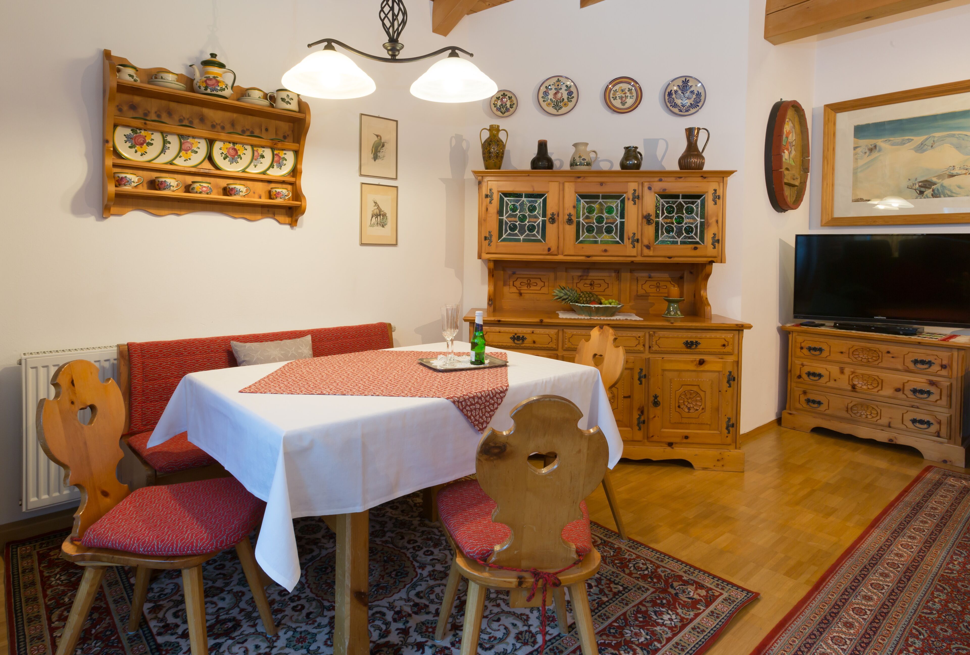 Ein Essbereich mit einem Tisch für zwei Personen, einer Holzkabine mit dekorativen Tellern und einem Fernseher in der Ecke.