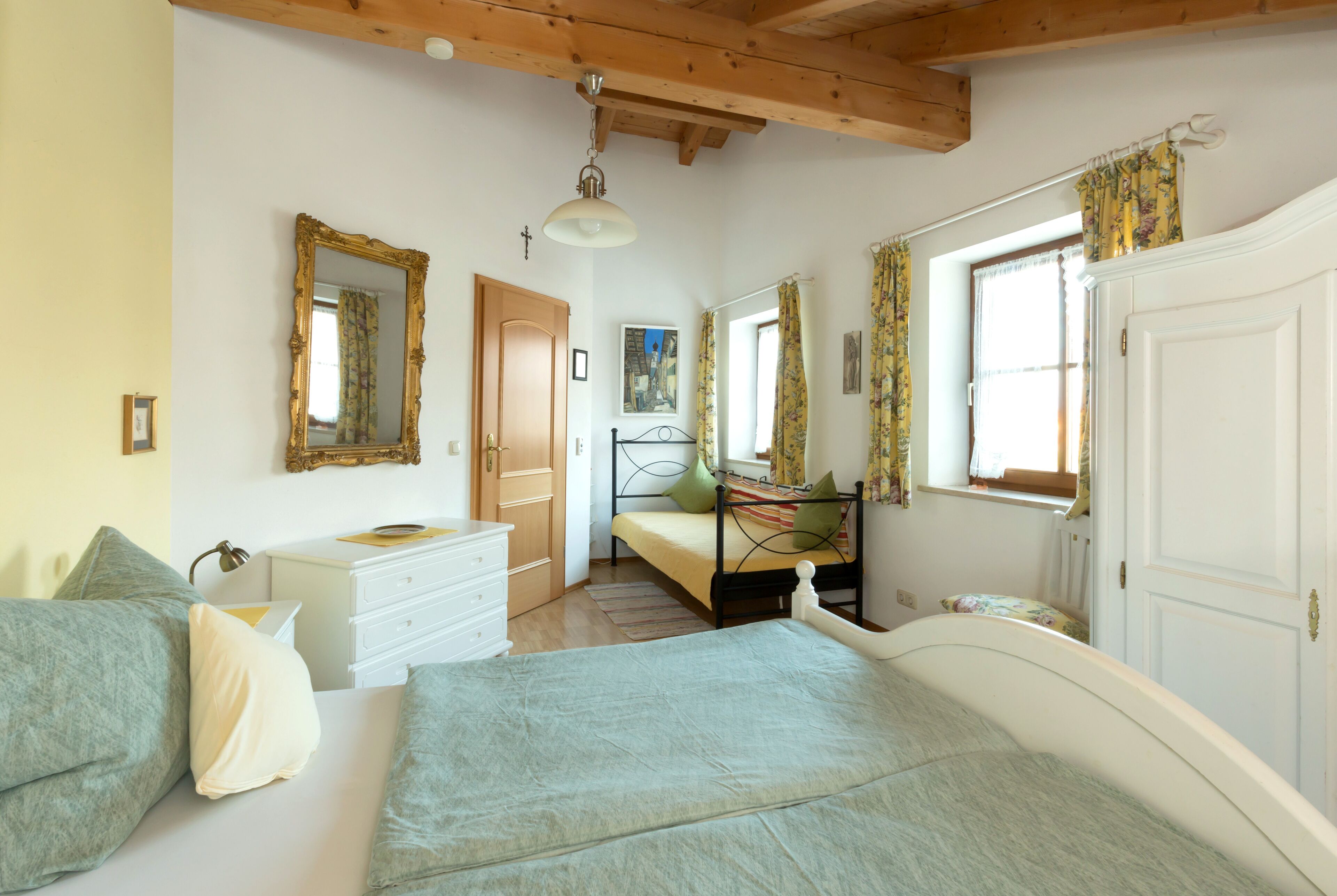 Un dormitorio con cama, cómoda, espejo, ventana con cortinas y puerta.