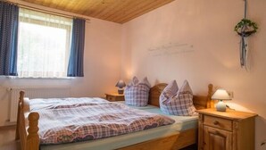 A cozy bedroom with a wooden bed, plaid bedding, a nightstand with a lamp, and a window with curtains. - Vacation apartment no. 2, 30 sqm, 1 bedroom, terrace, 4 stars, 3 pers. (Anger)