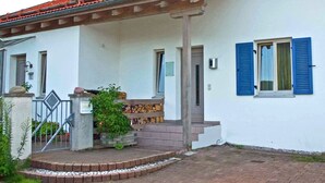 A white building with blue shutters, a tiled roof, and a small porch with steps leading to the entrance. - Ferienwohnung 50 qm, extra Schlafzimmer im Erdgeschoss° (Aschau im Chiemgau)