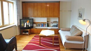 A living room with a wooden cabinet, a television, a sofa, a table with a white cloth, and a lamp. - Ferienwohnung 50 qm, extra Schlafzimmer im Erdgeschoss° (Aschau im Chiemgau)