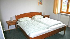 A double bed with a wooden frame, two bedside tables, a radiator, and a window with curtains. - Ferienwohnung 50 qm, extra Schlafzimmer im Erdgeschoss° (Aschau im Chiemgau)