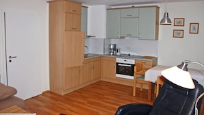 A compact kitchen with wooden cabinets, a dining table, and a chair. - Ferienwohnung 50 qm, extra Schlafzimmer im Erdgeschoss° (Aschau im Chiemgau)