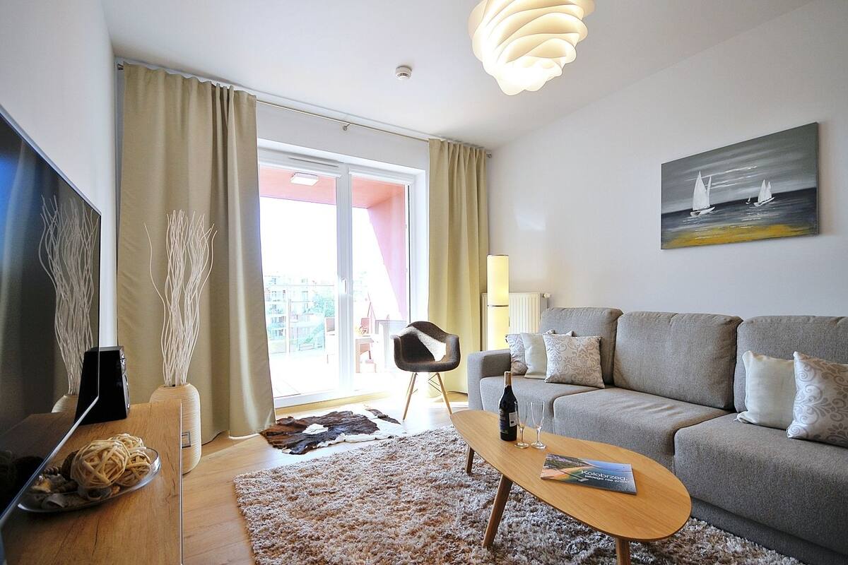 Ein modernes Wohnzimmer mit einem grauen Sofa, einem Couchtisch aus Holz, einem Fernseher und einem Gemälde von Segelbooten.