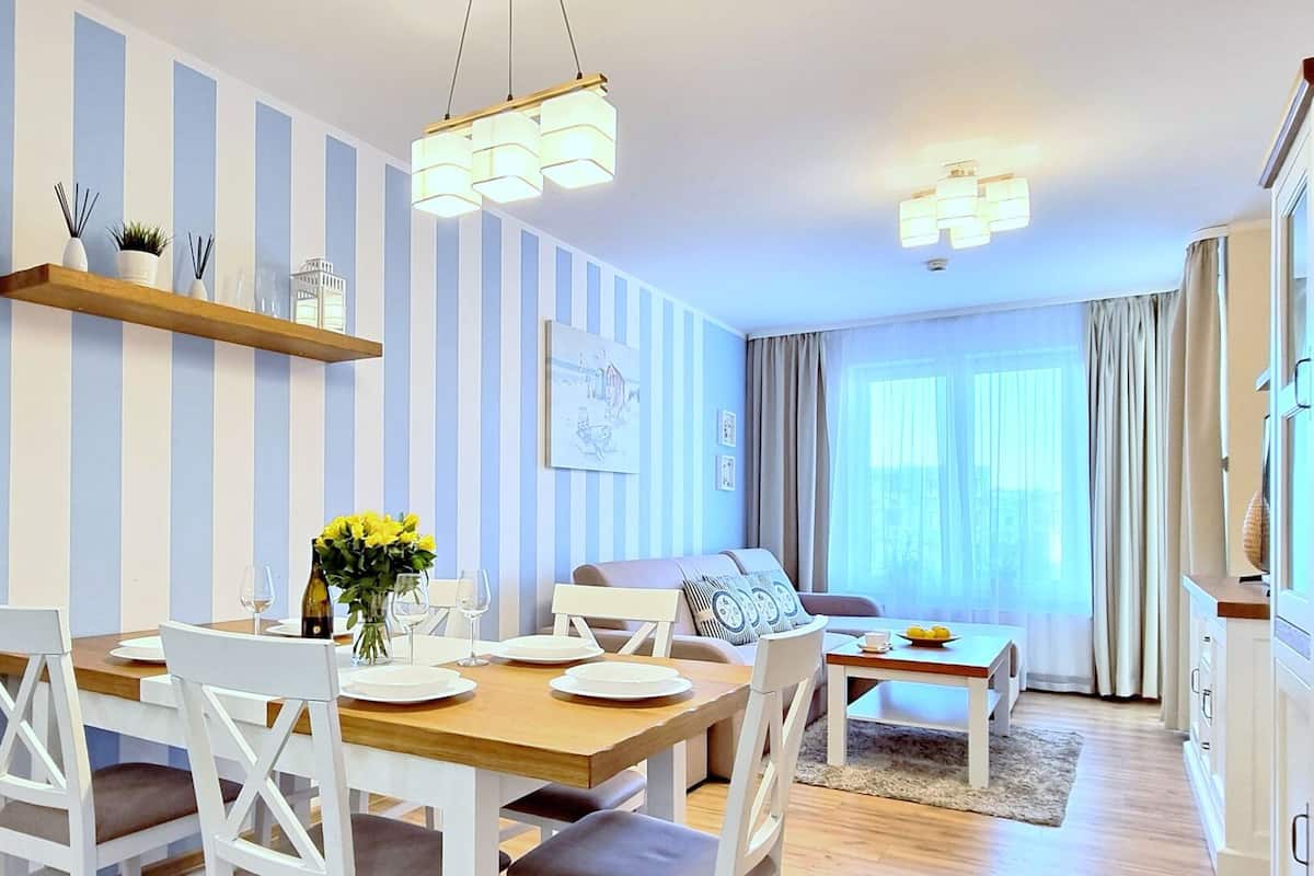 Ein Essbereich mit Holztisch, weißen Stühlen und einer hängenden Leuchte.