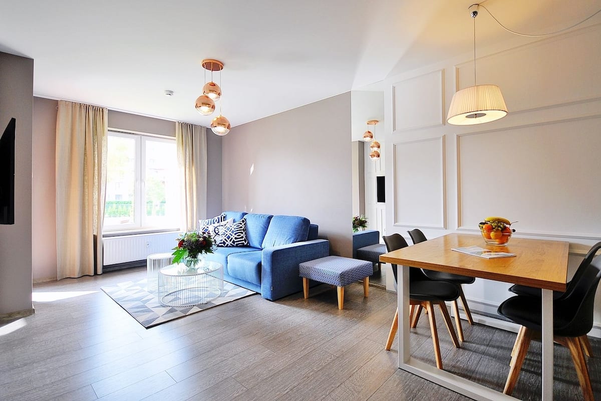 Ein modernes Wohnzimmer mit einem blauen Sofa, einem Holzespeisetisch mit Stühlen und einem großen Fenster mit Vorhängen.