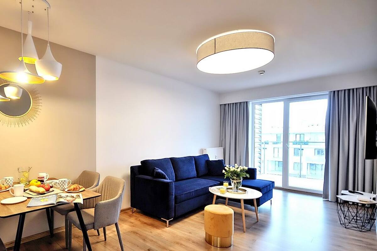 Ein modernes Wohnzimmer mit Essbereich, einer Couch und einem großen Fenster mit Vorhängen.
