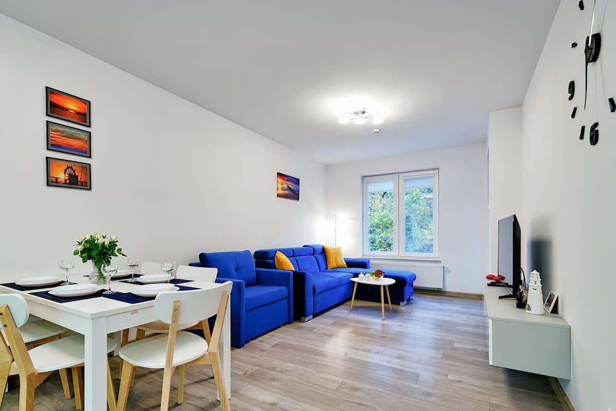Ein modernes Wohnzimmer mit Essbereich, einem blauen Sofa und einem Fernseher auf einem Lowboard.