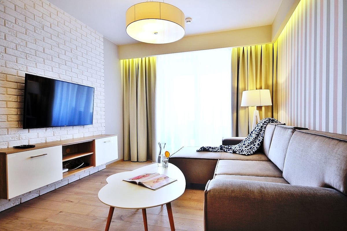 Ein modernes Wohnzimmer mit Flachbildfernseher, einer Couch, einem Couchtisch und einer Lampe.