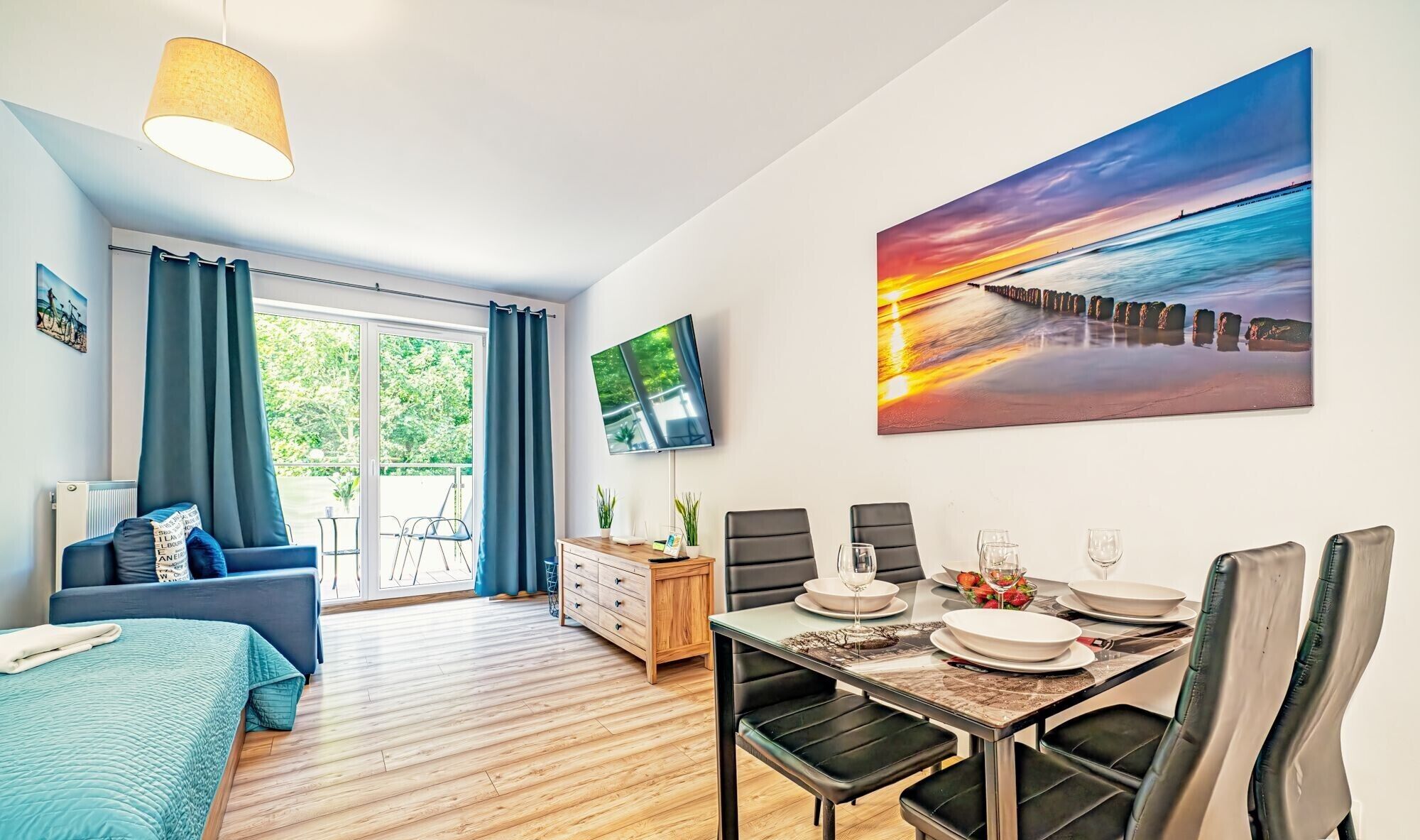 A modern room with a dining area, a TV mounted on the wall, and a large window with curtains.