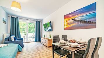 A modern room with a dining area, a TV mounted on the wall, and a large window with curtains.