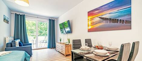 A modern room with a dining area, a TV mounted on the wall, and a large window with curtains.
