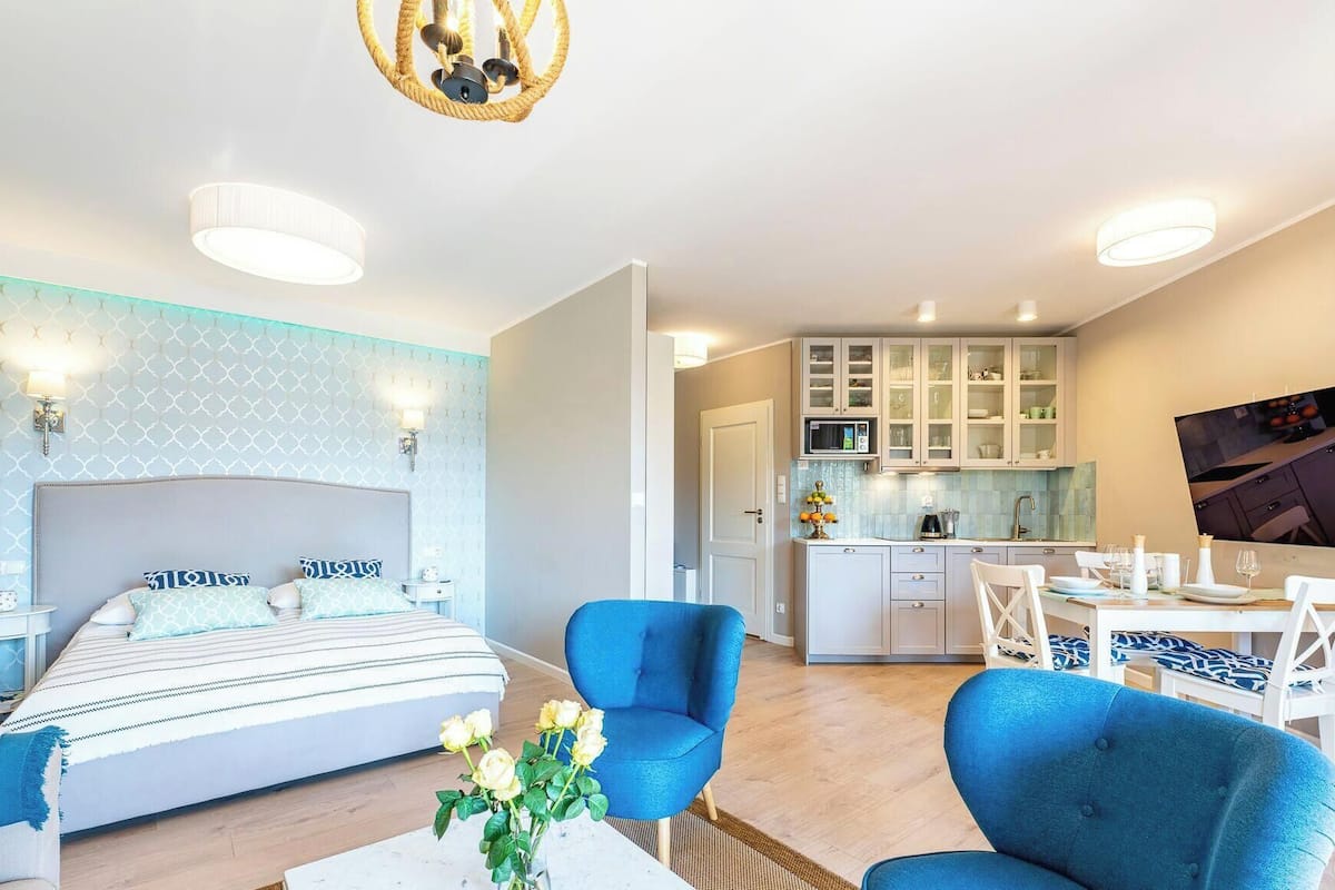 Ein modernes Hotelzimmer mit einem Bett, einem blauen Sessel, einem Essbereich und einer Küche.