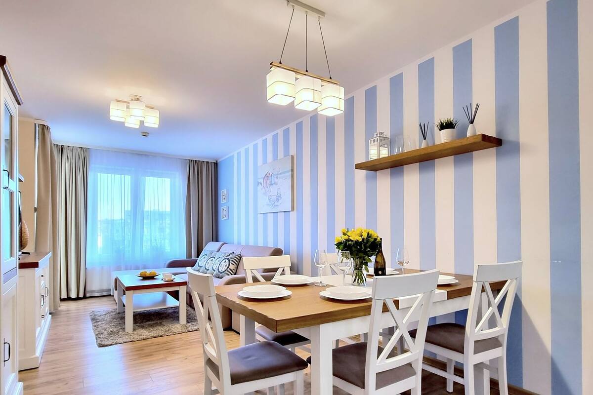 Ein moderner Essbereich mit einem Holztisch, gedeckt für vier Personen, weißen Stühlen und einer dekorativen Vase mit gelben Blumen.