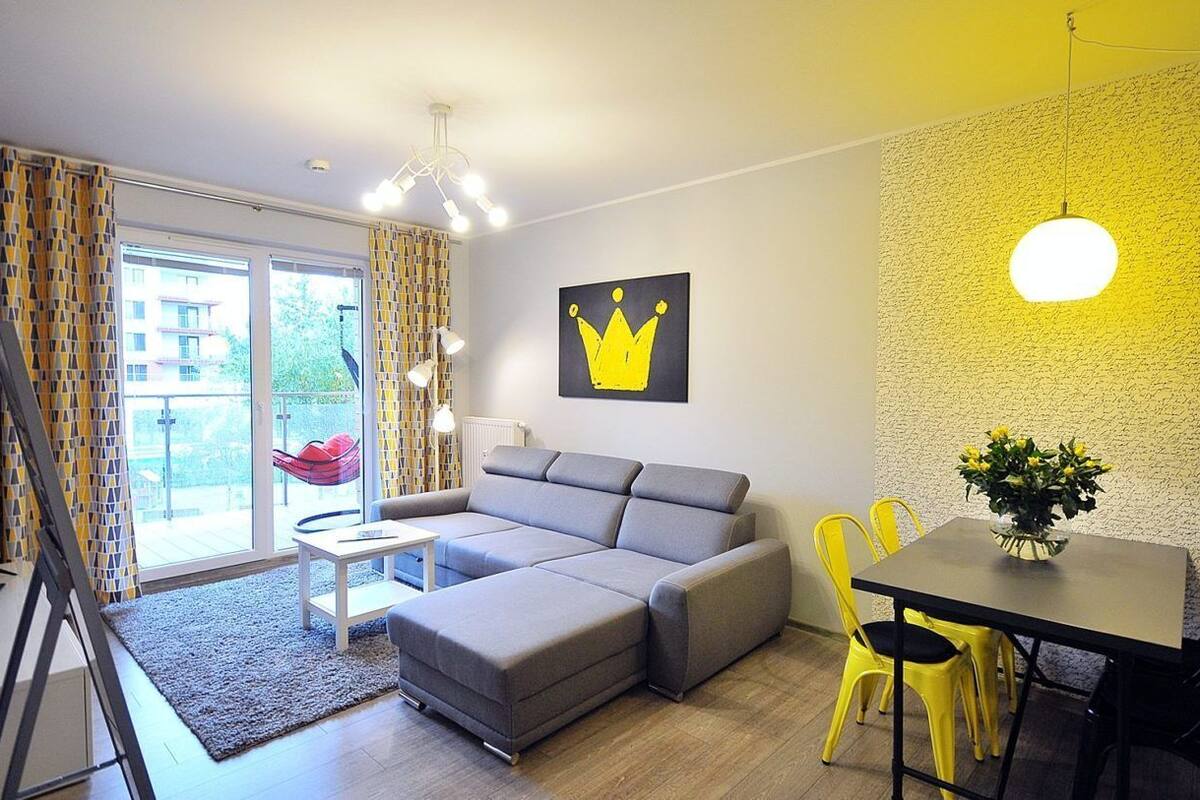 Ein modernes Wohnzimmer mit einem grauen Sofa, einem kleinen Tisch, gelben Stühlen und einem Esstisch mit einem Blumenstrauß.