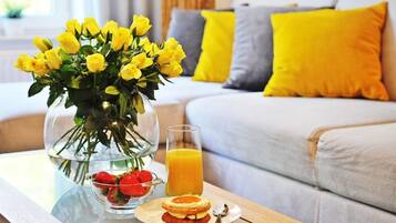 Une table mise pour le petit-déjeuner, avec un vase de fleurs jaunes, un verre de jus d’orange et une assiette de nourriture.