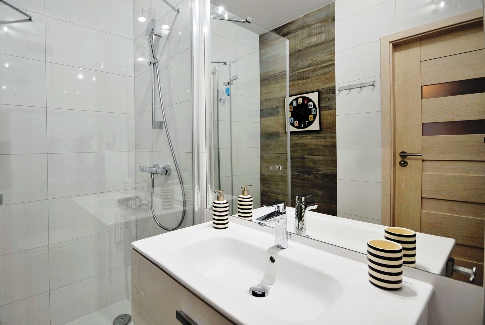 Une salle de bain moderne avec une douche à parois de verre, un lavabo blanc doté d’un robinet chromé et une porte en bois.