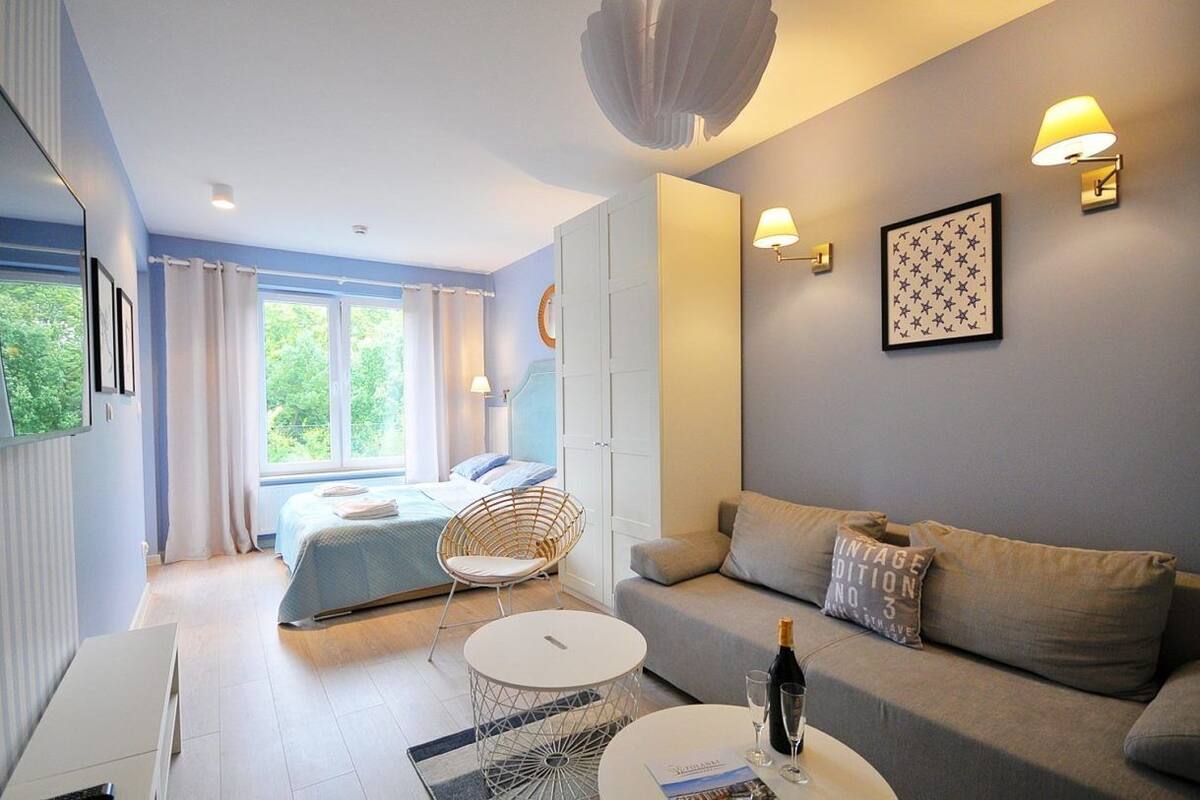 Ein modernes Schlafzimmer mit Bett, einer Sitzecke mit Sofa und Sessel, einem kleinen Tisch und einem fenster mit Vorhängen.